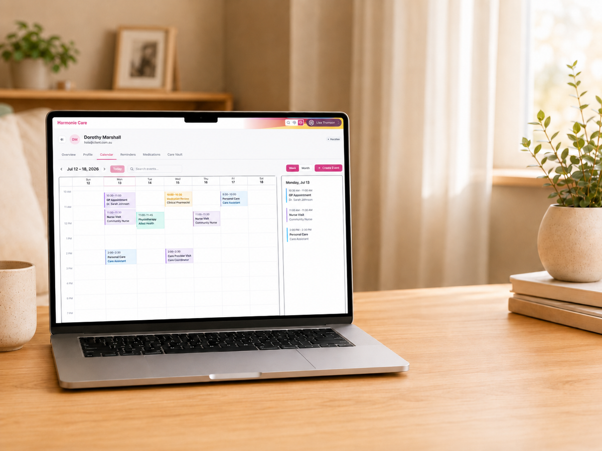 A silver laptop sits open on a wooden desk in a bright, modern room. The screen displays a colorful digital calendar or planner interface.