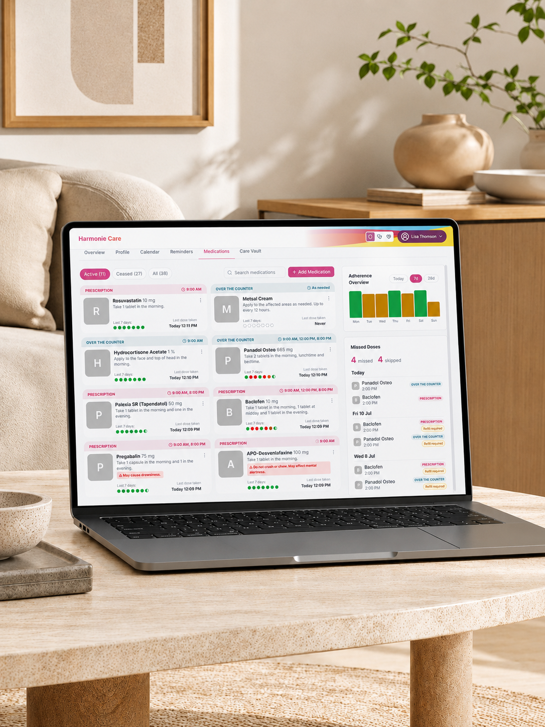 A laptop sits on a light wood table in a bright, modern living room. The laptop screen displays a colorful user interface dashboard with charts and data cards.