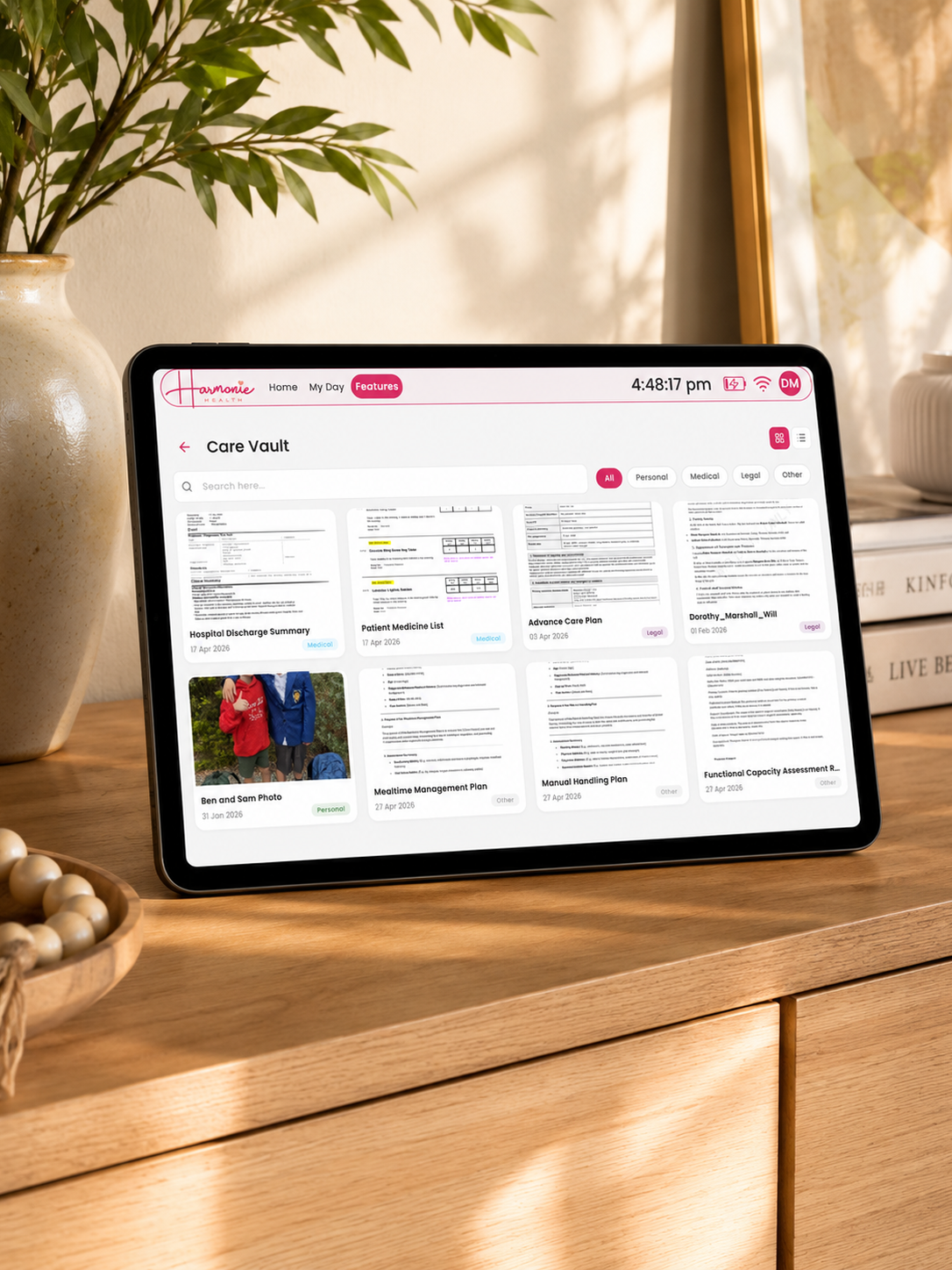 A tablet device displaying a digital document vault interface, placed on a wooden cabinet in a warm, sunlit room with a vase of greenery and books in the background.
