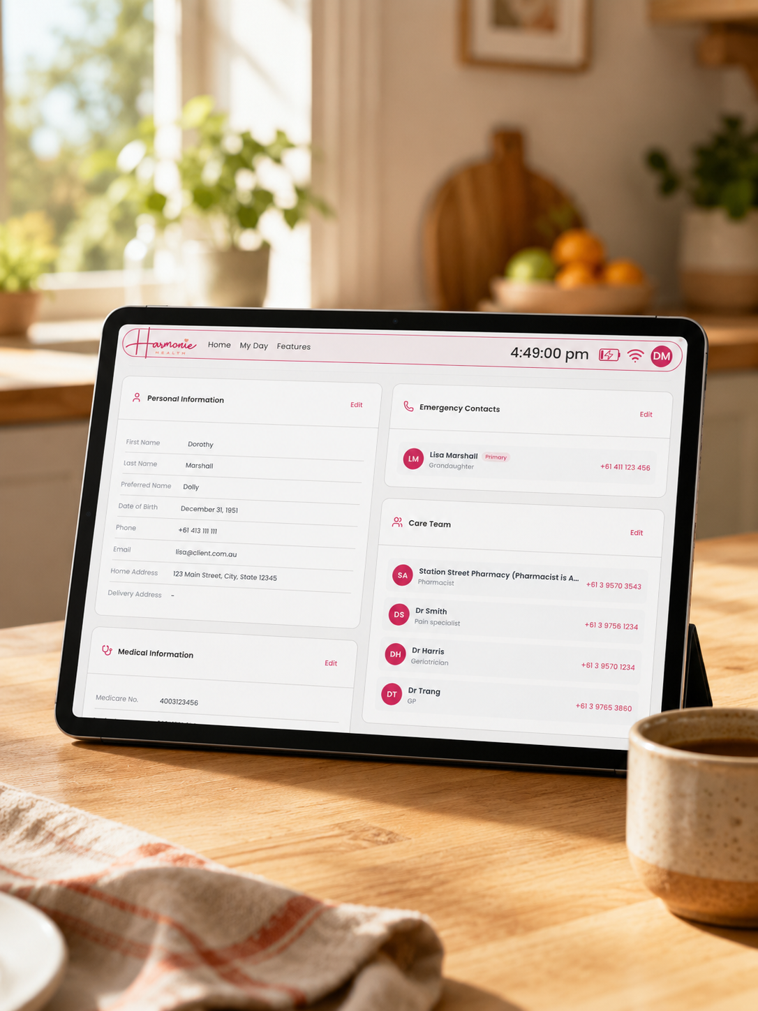 A tablet device on a wooden table in a warm kitchen setting, displaying a pink and white digital health or pharmacy dashboard interface.