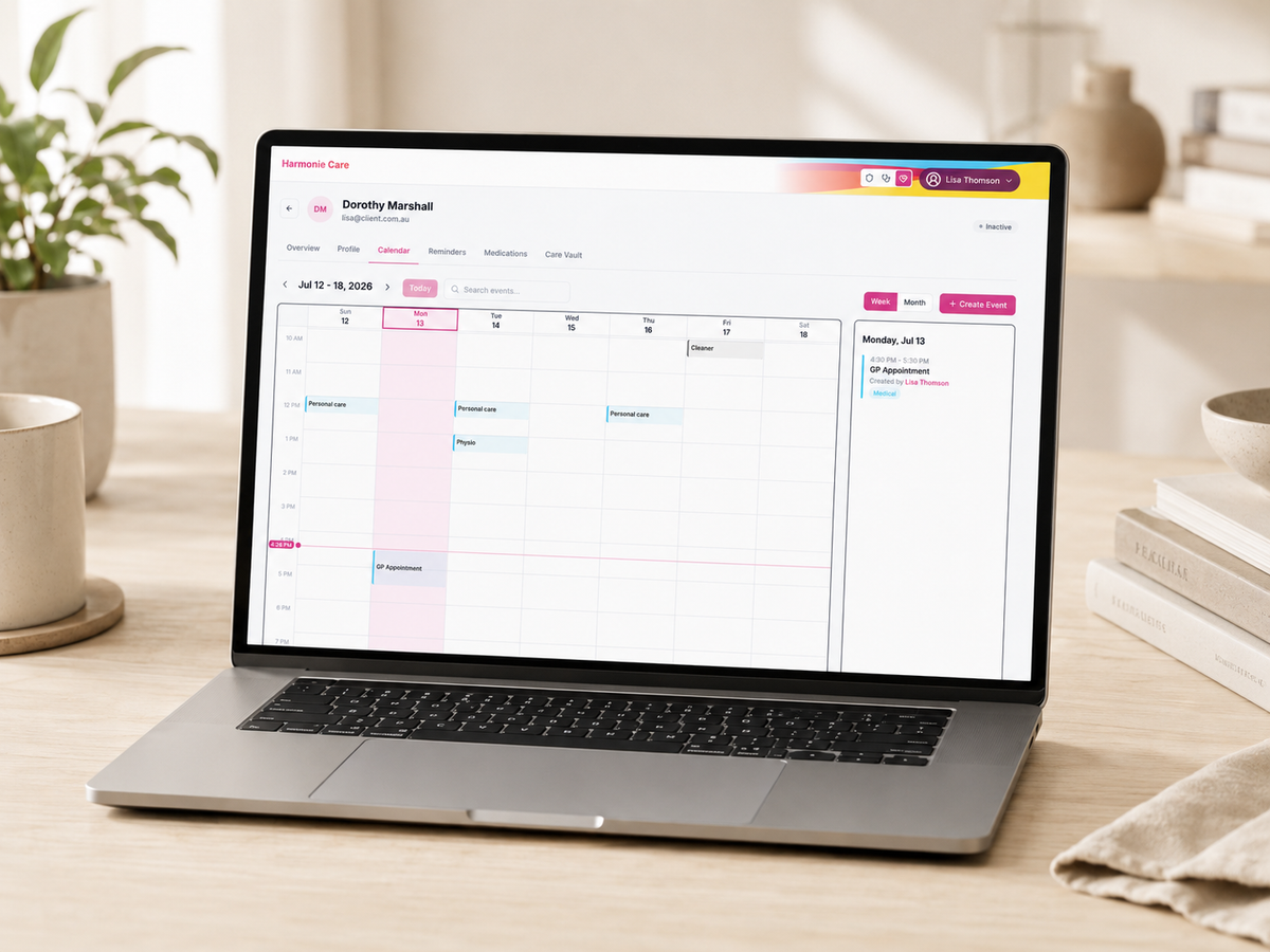 A silver laptop sits open on a light wood desk, displaying a digital calendar and task planner interface. The scene is styled with a potted plant, ceramic mugs, and books in a bright, modern room.
