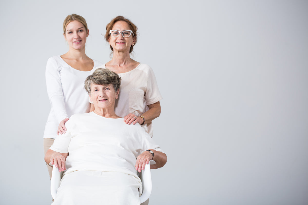 Three women in white clothing posing together against a plain light gray studio background.